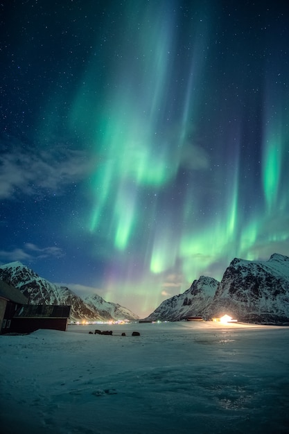 Fantástica Aurora boreal verde, luzes do norte com estrelas brilhando na montanha de neve no céu noturno no inverno nas Ilhas Lofoten, Noruega