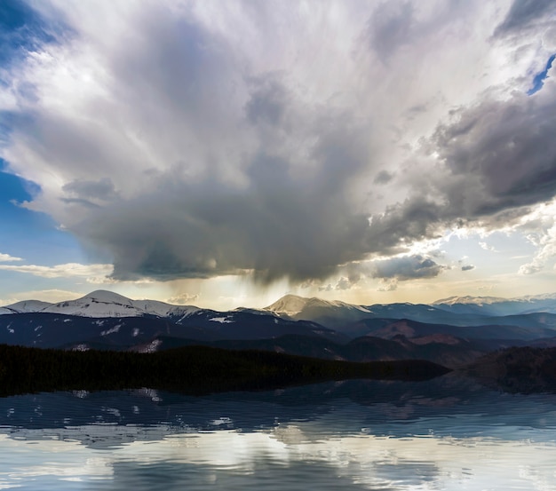 Fantástica vista de una enorme nube de tormenta blanca y oscura que cubre el cielo azul bajo sobre las montañas Hoverla y Petros en las montañas de los Cárpatos con nieve brillante en las cimas. Belleza y poder de la naturaleza.