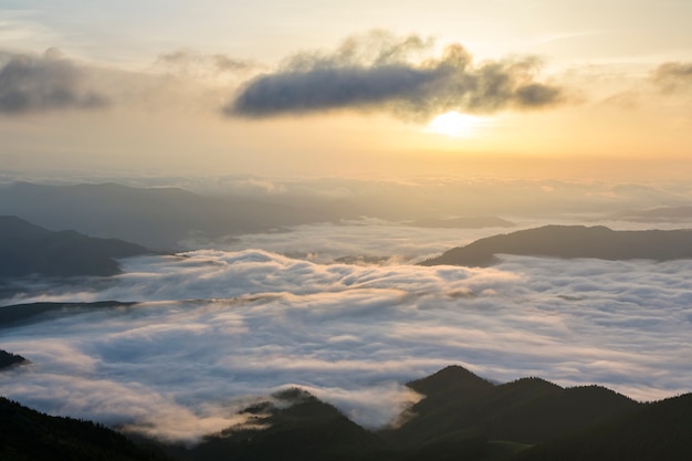 Fantástica vista del valle de montaña cubierto de nubes blancas y bajas como nubes de nieve que se extienden hasta el horizonte brumoso bajo el cielo brillante de la mañana con un resplandor naranja claro al amanecer. belleza del concepto de naturaleza.