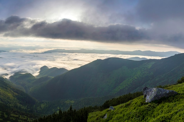 Fantástica vista del valle de montaña cubierto de nubes blancas y bajas como nubes de nieve que se extienden hasta el horizonte brumoso bajo el cielo brillante de la mañana con un resplandor naranja claro al amanecer. Belleza del concepto de naturaleza.