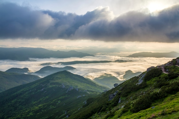 Fantástica vista del valle de montaña cubierto de nubes blancas y bajas como nubes de nieve que se extienden hasta el horizonte brumoso bajo el cielo brillante de la mañana con un resplandor naranja claro al amanecer. Belleza del concepto de naturaleza.