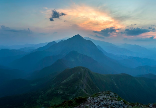 Fantástico nascer ou pôr do sol sobre o cume da montanha verde coberto com densa névoa azul. Sol laranja brilhante, elevando-se no céu nublado suave, no horizonte distante Beleza da natureza, turismo e conceito de viagem.