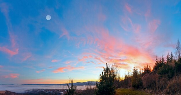 Fantástico paisaje al atardecer con nubes rosadas en el cielo y olas de nubes sobre las colinas.