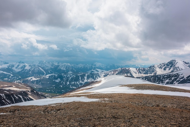 Fantastische alpine Landschaft mit schneebedeckten Bergen unter bewölktem Himmel. Malerische Berglandschaft in sehr großer Höhe bei bewölktem Himmel. Schöne stimmungsvolle Aussicht vom Steinhügel mit Schnee auf die schneebedeckte Bergkette