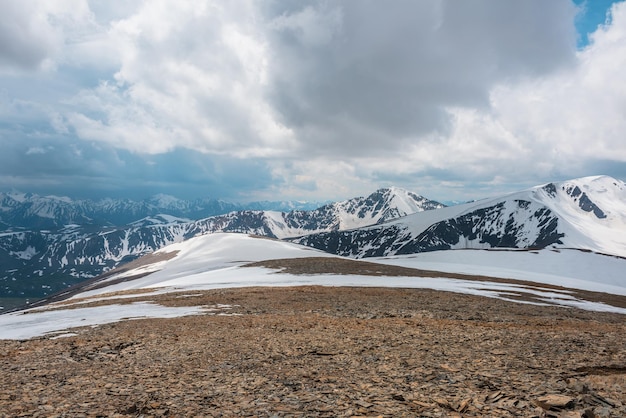 Fantastische alpine Landschaft mit schneebedeckten Bergen unter bewölktem Himmel. Malerische Berglandschaft in sehr großer Höhe bei bewölktem Himmel. Schöne stimmungsvolle Aussicht vom Steinhügel mit Schnee auf die schneebedeckte Bergkette