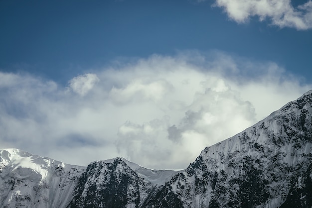 Fantastische Berglandschaft mit schwarz-weißer schneebedeckter Bergkette unter bewölktem Himmel. Minimalistische Hochlandlandschaft mit hoher Bergwand unter Wolken. Minimaler Blick auf wunderbaren Bergkamm.