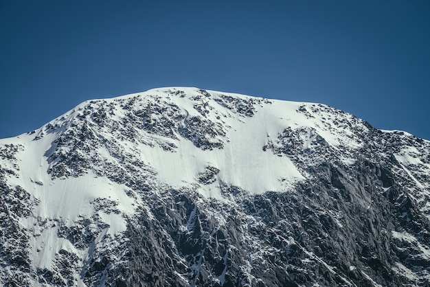 Fantastische Berglandschaft mit schwarz-weißer schneebedeckter Bergspitze im sonnigen blauen Himmel. Minimalistische Hochlandlandschaft mit Schneegesims auf hoher Bergwand. Minimaler Blick auf den wunderschönen schneeweißen Gipfel.