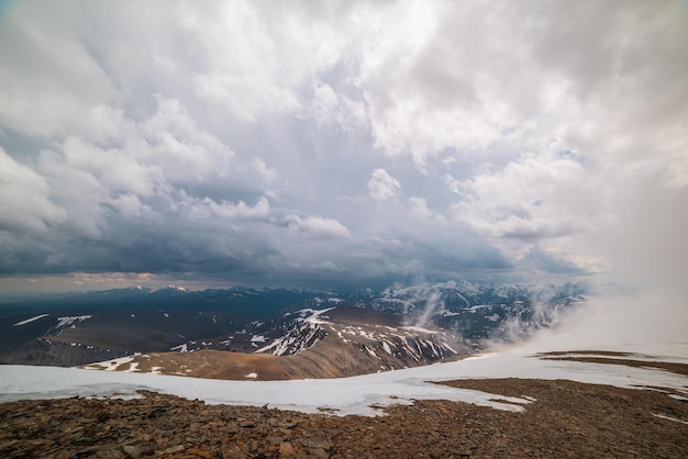 Fantastische Draufsicht durch Wolken zu hohen schneebedeckten Bergen Malerische Landschaft mit wunderschönen Schneebergen in niedrigen Wolken Atmosphärischer Alpenblick vom Steinhügel bis zur Schneebergkette mit niedrigen Wolken