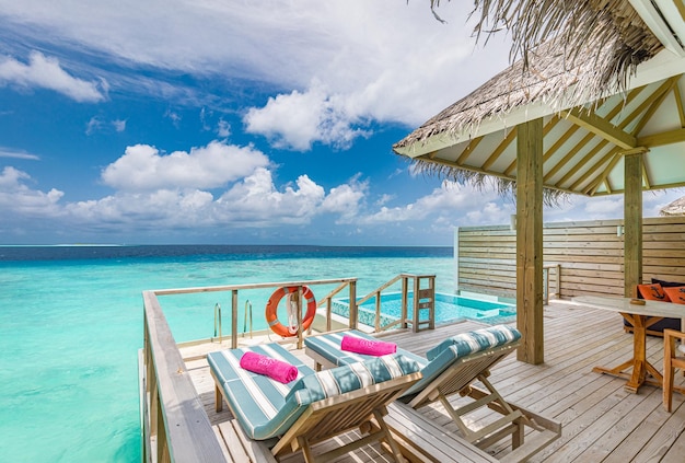 Fantastische Villa über dem Wasser, Terrasse mit Meerblick, Sonnenliegen, Stühle unter einem Sonnenschirm, luxuriöses Poolresort