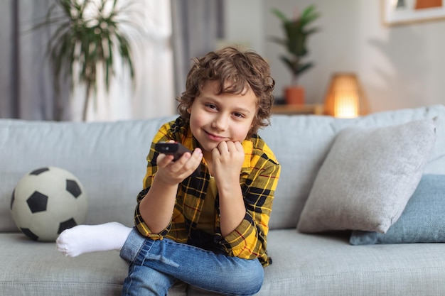 Fantastischer Kinderfernseher Lustiger kleiner Junge, der Videos oder Filme mit der Fernbedienung auswählt, die auf dem Sofa zu Hause sitzt, Fernseher pov