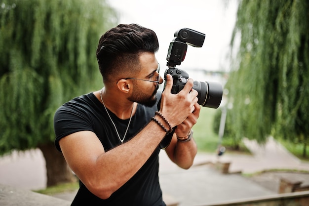 Fantastischer, schöner, großer arabischer Bart-Macho-Mann-Fotograf in Brille und schwarzem T-Shirt mit professioneller Kamera in der Hand