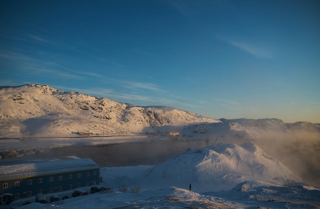 Farbenfroher Himmel bei Sonnenuntergang oder Sonnenaufgang in der Wintersaison schneebedecktes Feld und Nebel mit einem Himmel aus warmen Farbtönen bei Nebel im Morgengrauen