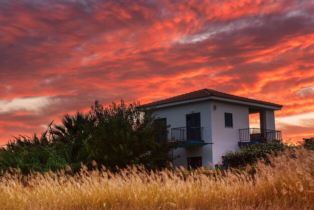 Farbenfroher, lebendiger Sonnenaufgang auf Zypern mit Haus und dramatischem Himmel