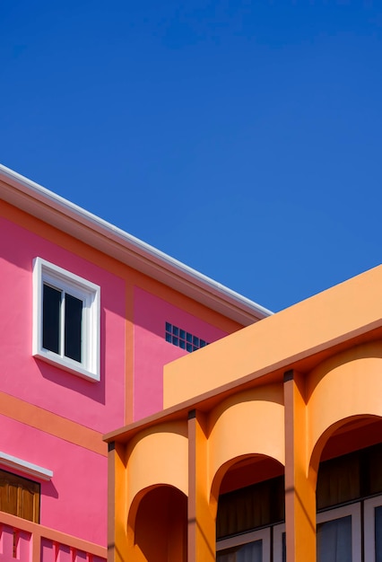 Farbenfrohes orangefarbenes Kolonnadenhaus mit rosafarbenem Gebäude vor blauem, klarem Himmel in perspektivischer Seitenansicht