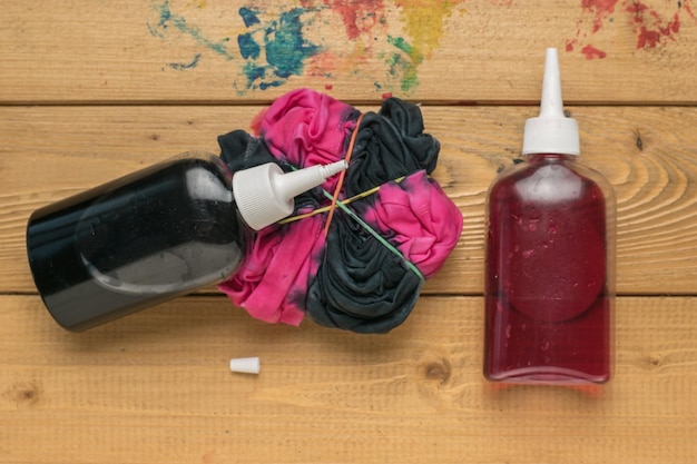 Farbflaschen und ein Rohling für ein Tie-Dye-T-Shirt auf Holzhintergrund Flach lag