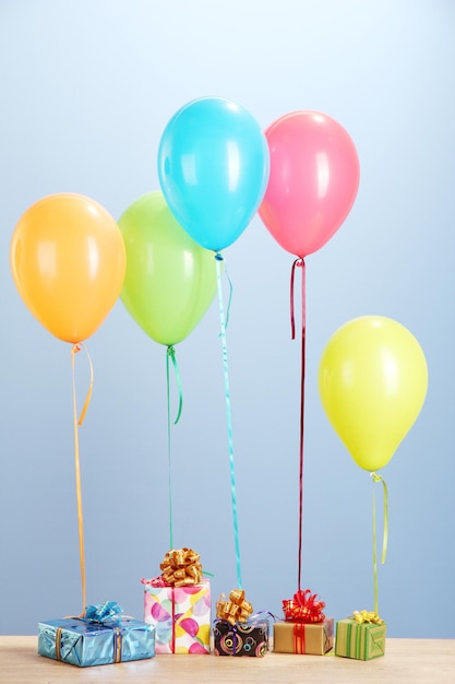 Farbige Ballons mit Geschenken auf einem Holztisch auf blauem Hintergrund