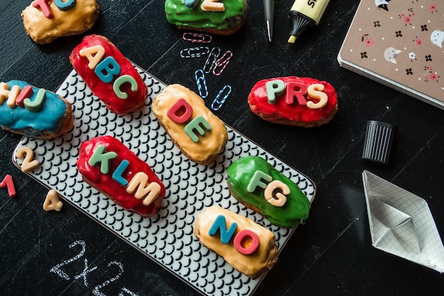 Farbige Eclairs Traditionelles französisches Dessert mit Buchstaben auf schwarzem Tisch neben Notizbuch und Planer Zurück zum Schulkonzept