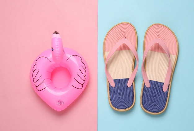 Farbige Flip-Flops und aufblasbare Flamingos auf blauem, pastellfarbenem Hintergrund. Strandurlaubskonzept flach liegend