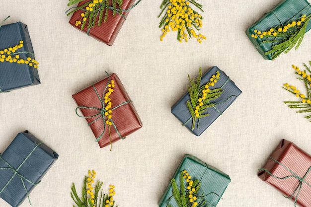 Farbige Geschenkkisten in handwerklichem Papier, geschmückt mit natürlichen Mimosa-Blüten, kreatives minimalistisches Muster, Frühlingsferien, Geschenke, Verpackung, Frauentag, Muttertag, Ostergrußkonzept, flach gelegt