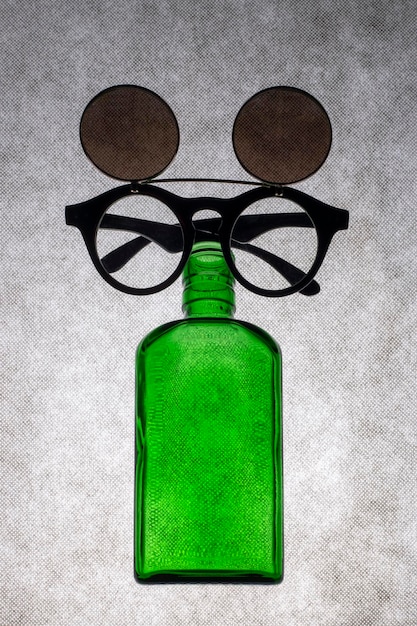 Farbige Glasflasche mit Sonnenbrille auf grauem Hintergrund