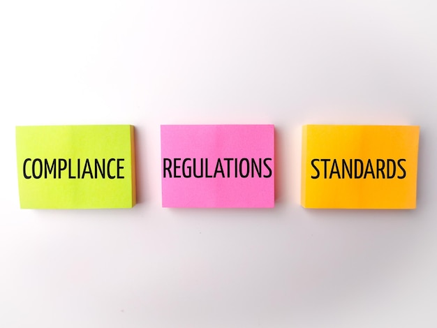 Farbige Haftnotiz mit dem Wort COMPLIANCE REGULATIONS STANDARDS