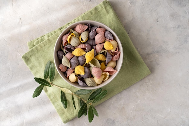 Farbige italienische Pasta Conchiglie oder Muscheln in Schüssel auf grüner Serviette und konkretem Hintergrund