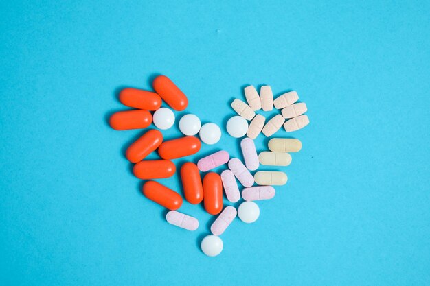 Foto farbige medizin pillen in herzform, isoliert auf blauem hintergrund, vitaminergänzung farbenfroh