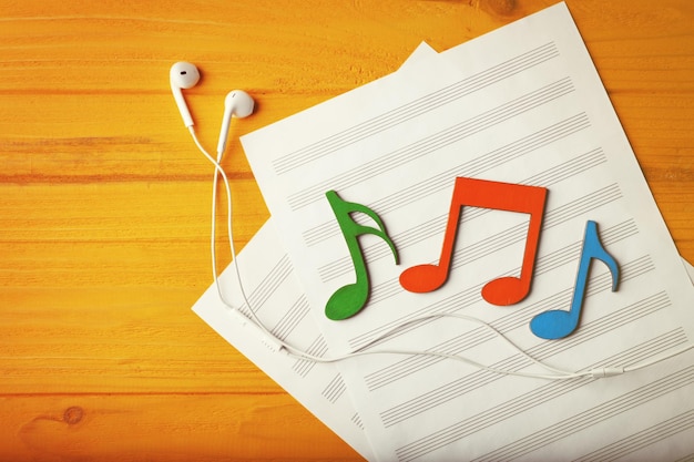 Farbige Musiknoten und Kopfhörer liegen auf einem Musikblatt auf gelbem Holzhintergrund
