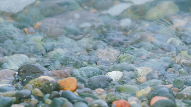 Farbige Seegesteine, kleine Schaumwellen, die auf einem Kiesstrand brechen