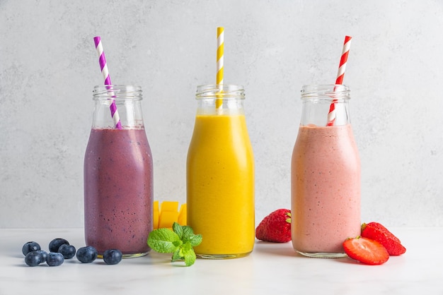 Farbige Sommerfrucht- und Beeren-Smoothie-Getränke oder Milchshake in Flaschen mit Strohhalm auf weißem Hintergrund