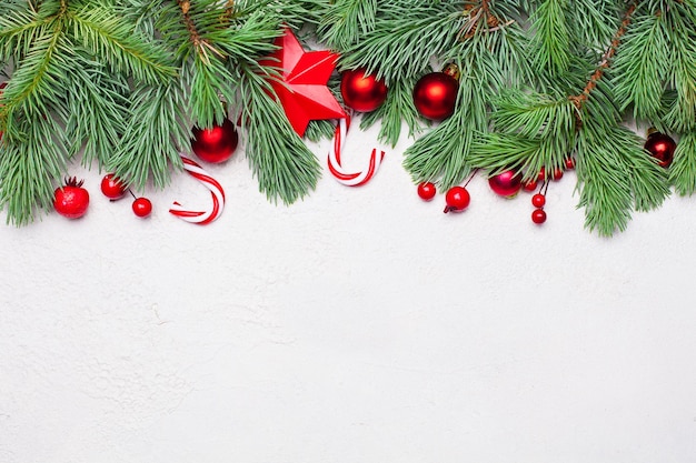 Farbige Weihnachtskomposition mit grünem Weihnachtstannenzweig, roten Stechpalmenbeeren und Kugeln auf weißem Stuckputz-Texturhintergrund. Weihnachtsrand, Draufsicht flach mit Kopierraum