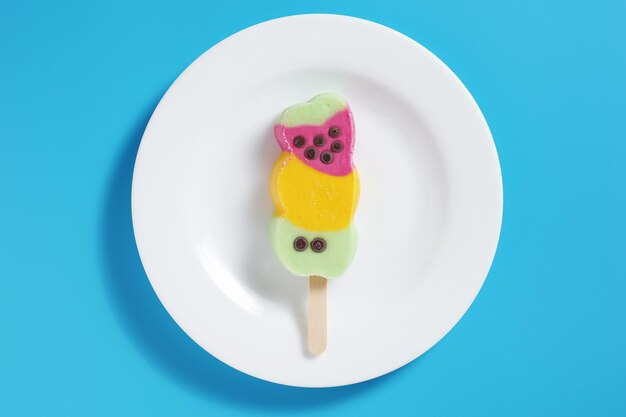 Farbiges Obst-Popsicle auf einem Teller auf blauem Hintergrund