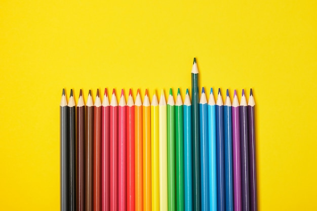 Farbstifte auf gelbem Hintergrund Draufsicht ein Bleistift fällt auf