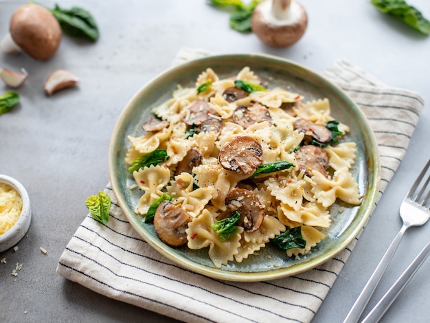 Farfalle com cogumelos e espinafres numa superfície de concreto cinza. Macarrão vegetariano. imagem horizontal, close-up