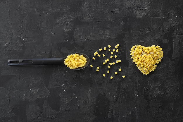 Foto farfalle de macarrão cru na colher de pau em fundo preto vista superior do ingrediente da culinária italiana