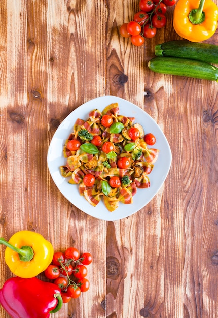 Farfalle de massa italiana em molho de tomate e vários tipos de legumes em uma mesa de madeira