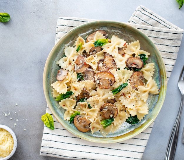 Farfalle macarrão com cogumelos e espinafre, servido em um prato de cerâmico. Superfície cinza. Cozinha mediterrânea. vista do topo.