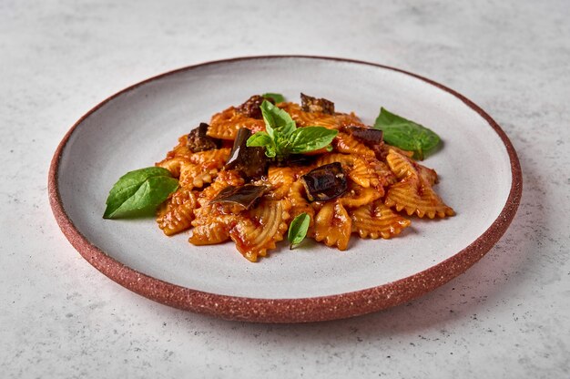 Farfalle de pasta con berenjena salsa de tomate, queso y albahaca en un plato sobre un fondo de textura gris