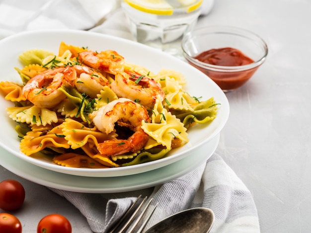 Farfalle pasta con camarones sobre un fondo gris claro.