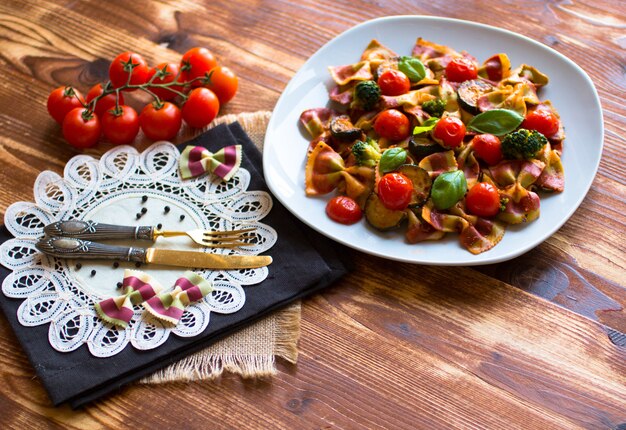 Foto farfalle de pasta italiana en salsa de tomate y varios tipos de verduras en una mesa de madera