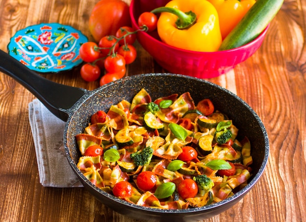 Farfalle de pasta italiana en salsa de tomate y varios tipos de verduras en una mesa de madera