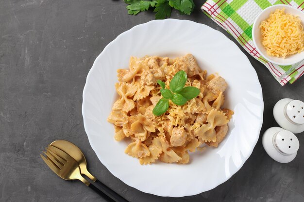 Farfalle de pasta con pavo en salsa de crema de tomatosour servido queso y albahaca en un plato blanco sobre un fondo gris Vista superior