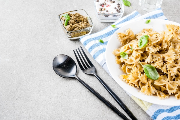 Farfalle con salsa de pesto y hojas de albahaca en plato blanco