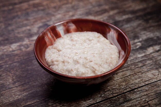 Farinha de aveia com leite de coco em fundo escuro de madeira. Saúde alimentar tradicional em prato marrom em forma de coração com mingau. Dieta de comida saudável deliciosa. Copie o espaço