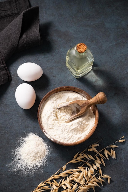 Farinha de aveia em uma tigela de madeira com ovos e oli em um fundo escuro Farinha orgânica natural para panificação caseira