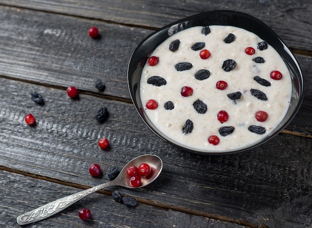 Farinha de aveia em uma tigela preta com passas e cranberries em uma mesa de madeira escura.