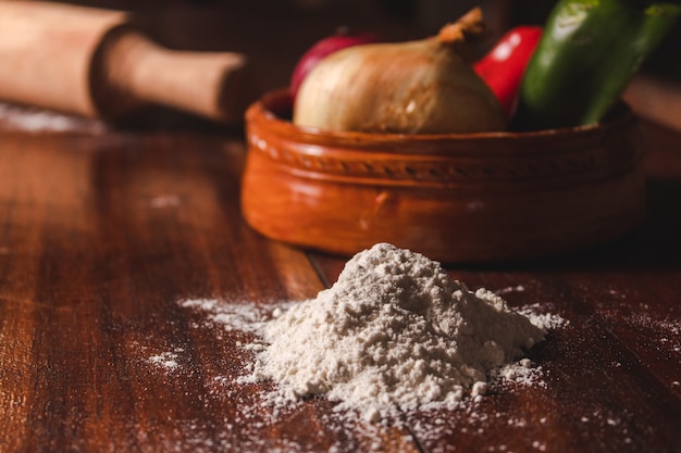 Foto farinha derramada ao lado dos ingredientes em uma mesa de madeira.