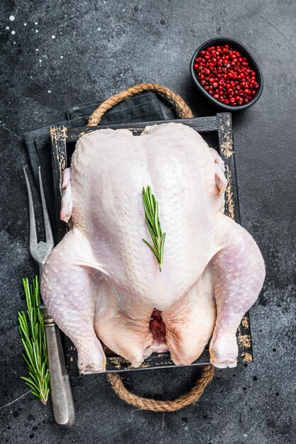 Farm Rohes ganzes Huhn in einem Holztablett. Schwarzer Hintergrund. Ansicht von oben.