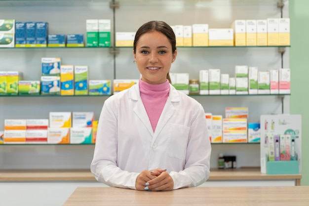 Farmacéutica joven mirando a la cámara en una farmacia con productos en estantes en el fondo