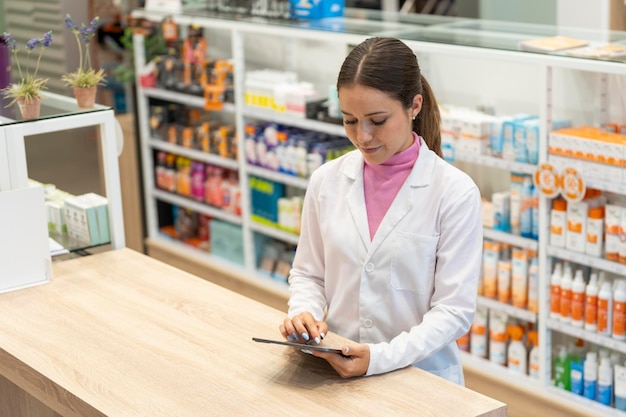 Farmacéutica joven mirando la pantalla de una tableta digital en la farmacia